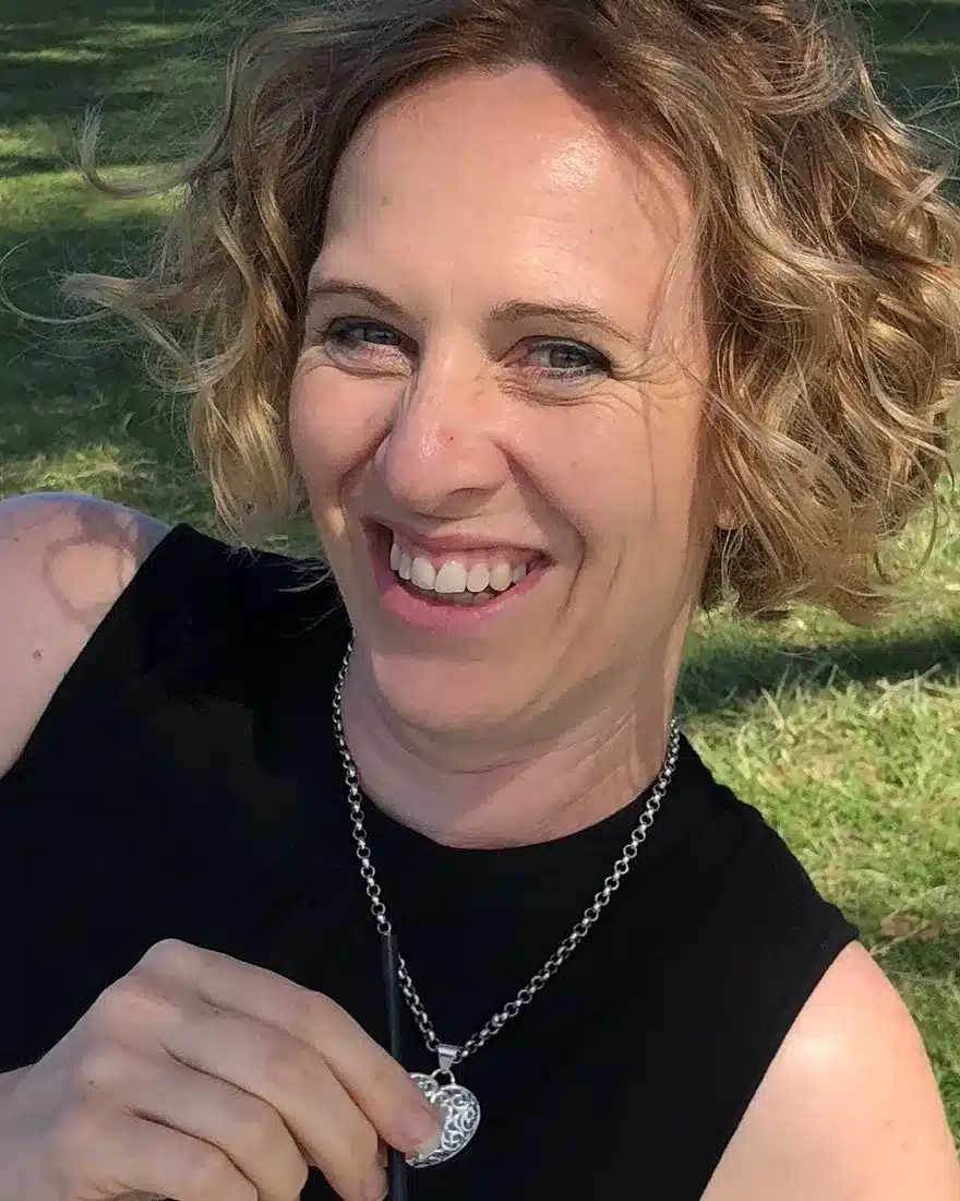 Anita, smiling, sitting on the grass on a sunny day